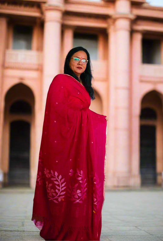 Woman in a red saree standing in a room with patterned walls and a blue door.